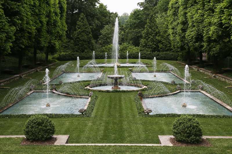 Longwood Gardens formal fountain garden with symmetrical pools, arcing water jets, clipped lawns, and tall tree-lined paths stretching outward gracefully.
