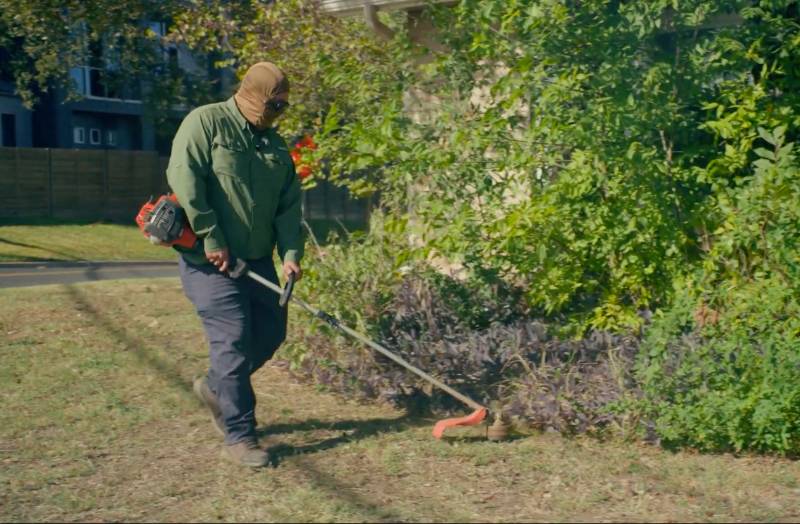 LawnStarter pro Carlos string trims grass around a residential landscape bed during a standard mowing and edging service.