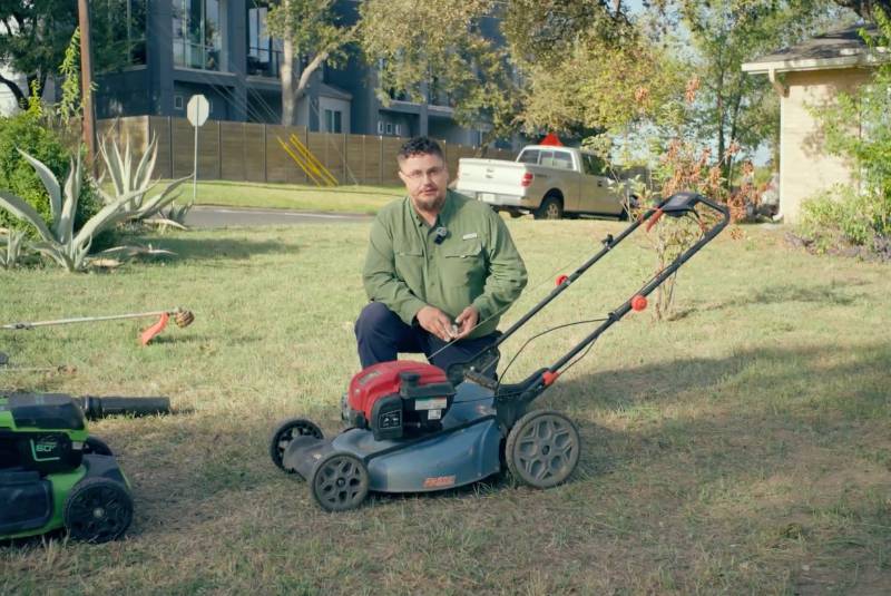 LawnStarter pro Carlos Garza kneels beside a lawn mower in a residential yard before completing a first-time mowing service.