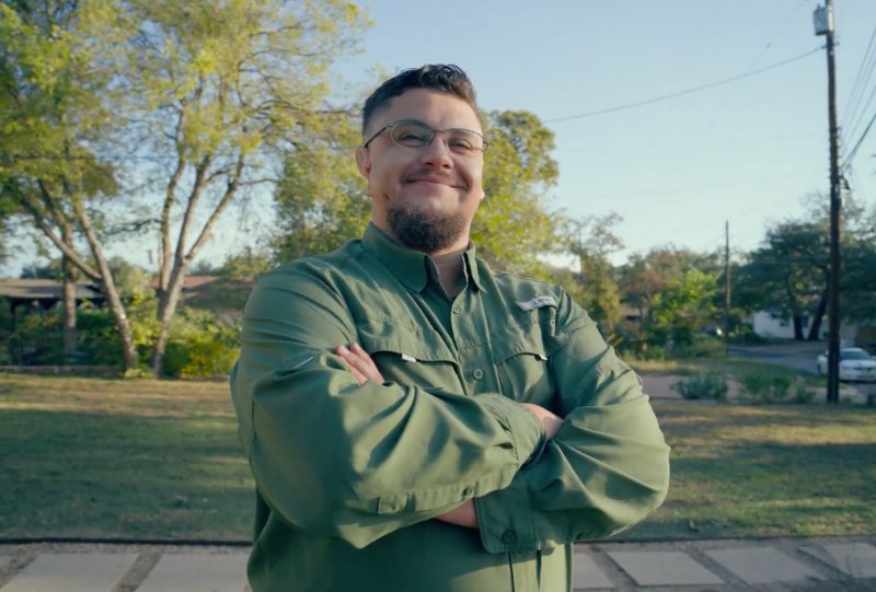 LawnStarter pro Carlos stands smiling with arms crossed in a residential yard after completing lawn care work.