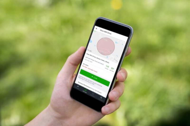 Hand holding smartphone showing a lawn care quote screen with property map, pricing details, and green lawn background.