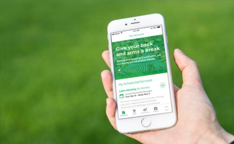 LawnStarter's customer app, photo of hand holding phone with green field with white letters that read Give Your Back and Arms a Break as the headline on a leaf cleanup services page