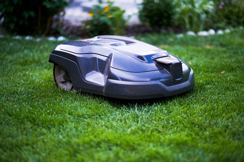 Gray robotic lawn mower cutting thick green grass in a backyard