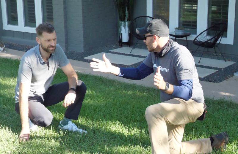 LawnStarter pro Justin Stultz talks with a homeowner in a shaded front yard after completing residential lawn care work.
