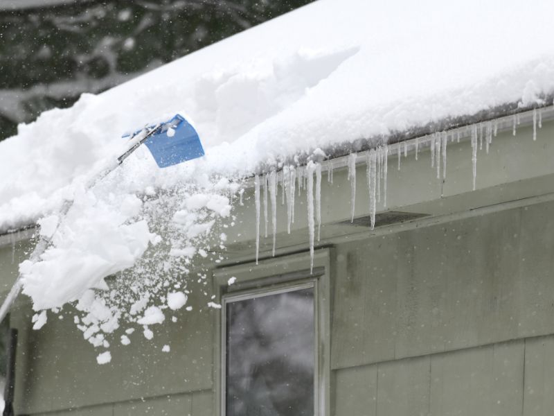 removing snow on the roof after snow storm using a roof rake