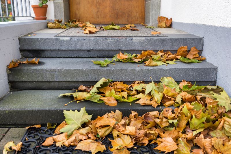 Fallen yellow, orange, and green autumn leaves pile up on gray stone entry steps and doormats leading to a wooden front door, creating a slipping hazard.